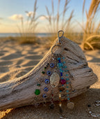 Ariel La Boutique beaded bag charm with evil eye motifs, silver charms, and glass beads on driftwood at the beach.