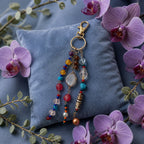 Ariel La Boutique bohemian beaded keychain with multi-colored crystals and stones on a blue velvet pillow with orchids