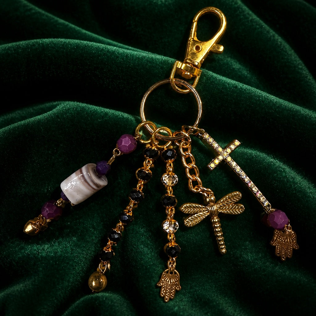 Ariel La Boutique beaded charm keychain with gold-tone cross, dragonfly, and Hamsa hand motifs on green velvet.