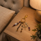 Ariel La Boutique beaded charm keychain with gold-tone cross, dragonfly, and Hamsa hand motifs on a wooden nightstand.
