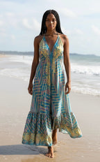 Ariel La Boutique bohemian maxi dress with halter neck and geometric print in blue, yellow, and purple on a beach.