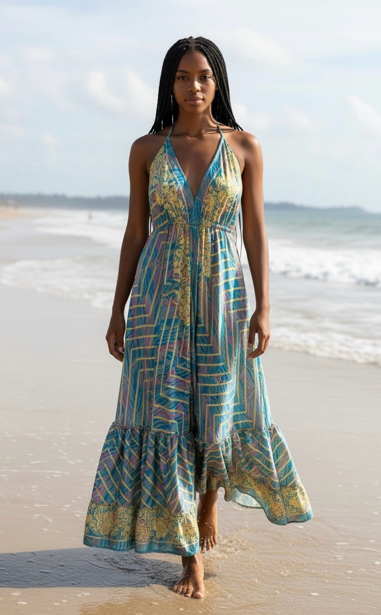 Ariel La Boutique bohemian maxi dress with halter neck and geometric print in blue, yellow, and purple on a beach.