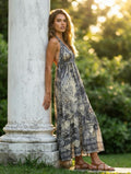 Ariel La Boutique bohemian maxi dress with halter neck and earthy print, worn by a woman leaning against a stone pillar