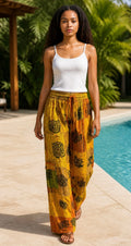Ariel La Boutique bohemian wide-leg cargo pants in yellow and orange patchwork with floral print by a pool.