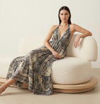Ariel La Boutique bohemian maxi dress with a halter neck and earthy print, worn by a woman on a cream bouclé sofa.
