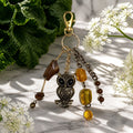 Ariel La Boutique owl keychain with antique bronze charm, amber beads, and gold-tone clasp on a marble surface.