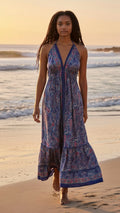 Ariel La Boutique bohemian halter maxi dress with blue and pink paisley print, worn by a model on a beach at sunset.