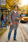 Ariel La Boutique unisex hooded poncho with geometric patterns, fringe hem, and kangaroo pocket worn at a bus stop.